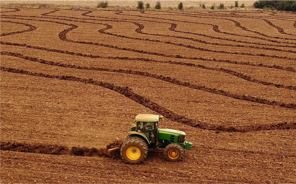 Trator preparando o solo em área agrícola com linhas de cultivo